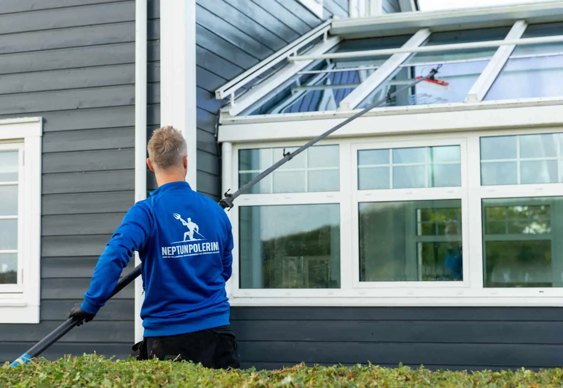 Vinduesvask med rentvandsanlæg og teleskopstang på et hus med glasoverdækning